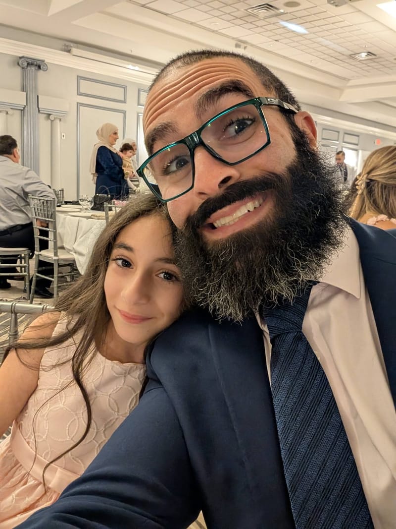 Abe in a suit and tie leaning in for a selfie with one of his daughters at a formal event.