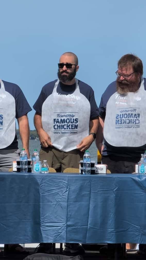 Abe at a competitors table in a contest bib, water bottles lined up in front of him, another competitor alongside.